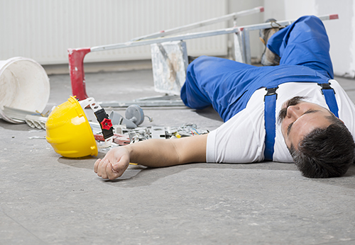 Construction worker injured and lying on the floor next to a fallen ladder and hard hat, discussing a personal injury case going to trial